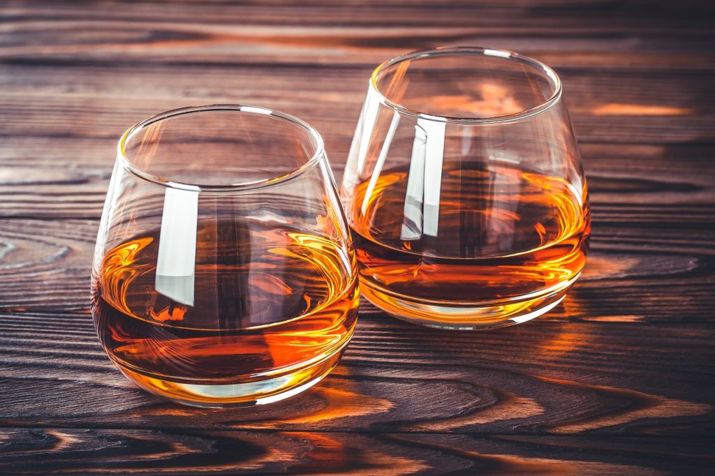 Deux verres de whisky sur une table en bois brun foncé.